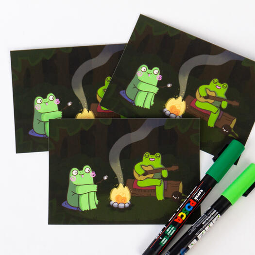 Two frogs and a tadpole sitting at a campfire in the forest.